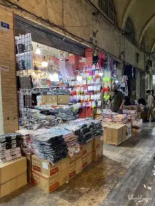 لباس‌های زیر چیده شده در جلوی یک مغازه در بازار آل یاسین بازار و مرد فروشنده در کنارشان ایستاده