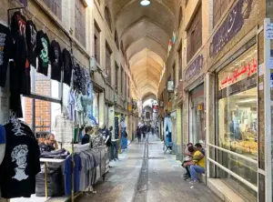 تصویر ویترین مغازه‌ها و مردم نشسته روی پله مغاز‌ه‌ها در بازار مسقف آهنگرهای بازار تهران