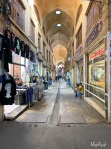 تصویر ویترین مغازه‌ها و مردم نشسته روی پله مغاز‌ه‌ها در بازار مسقف آهنگرهای بازار تهران