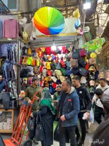 مردم در حال تردد در چهارسوق کوچک بازار از جلوی یک مغازه کلاه‌فروشی