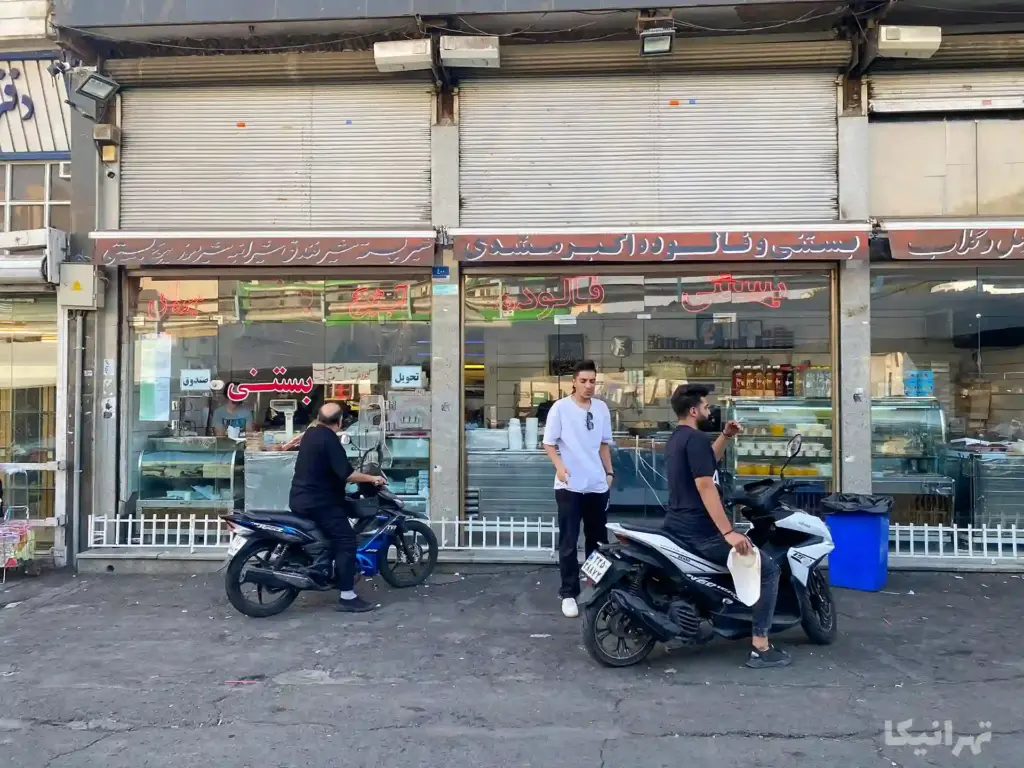 چند مشتری سوار بر موتور جلوی بستنی فروشی اکبرمشدی ایستادهاند.