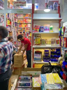 فروشنده درحال جابجایی جعبه‌ها در مغازه کوچک لوازم تحریری در بازار بین الحرمین