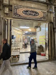چند نفر در حال تردد درون و در مقابل سرای اکبریه در کوچه کبابی‌های بازار