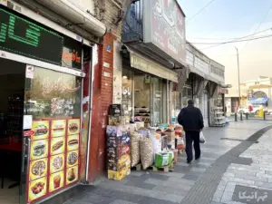 مردی در خال عبور از کنار مواد غذایی چیده شده در مقابل مغازه‌ای در میدان محمدیه