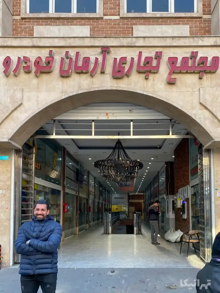 مردی جلوی پاساژ آرمان چراغ برق ایستاده به دوربین لبخند می‌زند