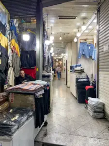 فروشنده‌ای در حال کار با موبایل داخل مغازه کوچک خود در پاساژ استاد شهریار بازار