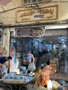 چند نفر در حال تردد در پاساژ الغدیر کوچه معظم بازار و دو نفر در حال خالی‌کردن بار از روی چرخ در جلوی ورودی پاساژ