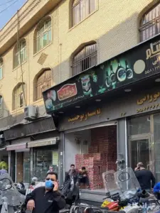 چند نفر در حال تردد یا نشسته جلوی پاساژ توحید کوچه احمدی بازار