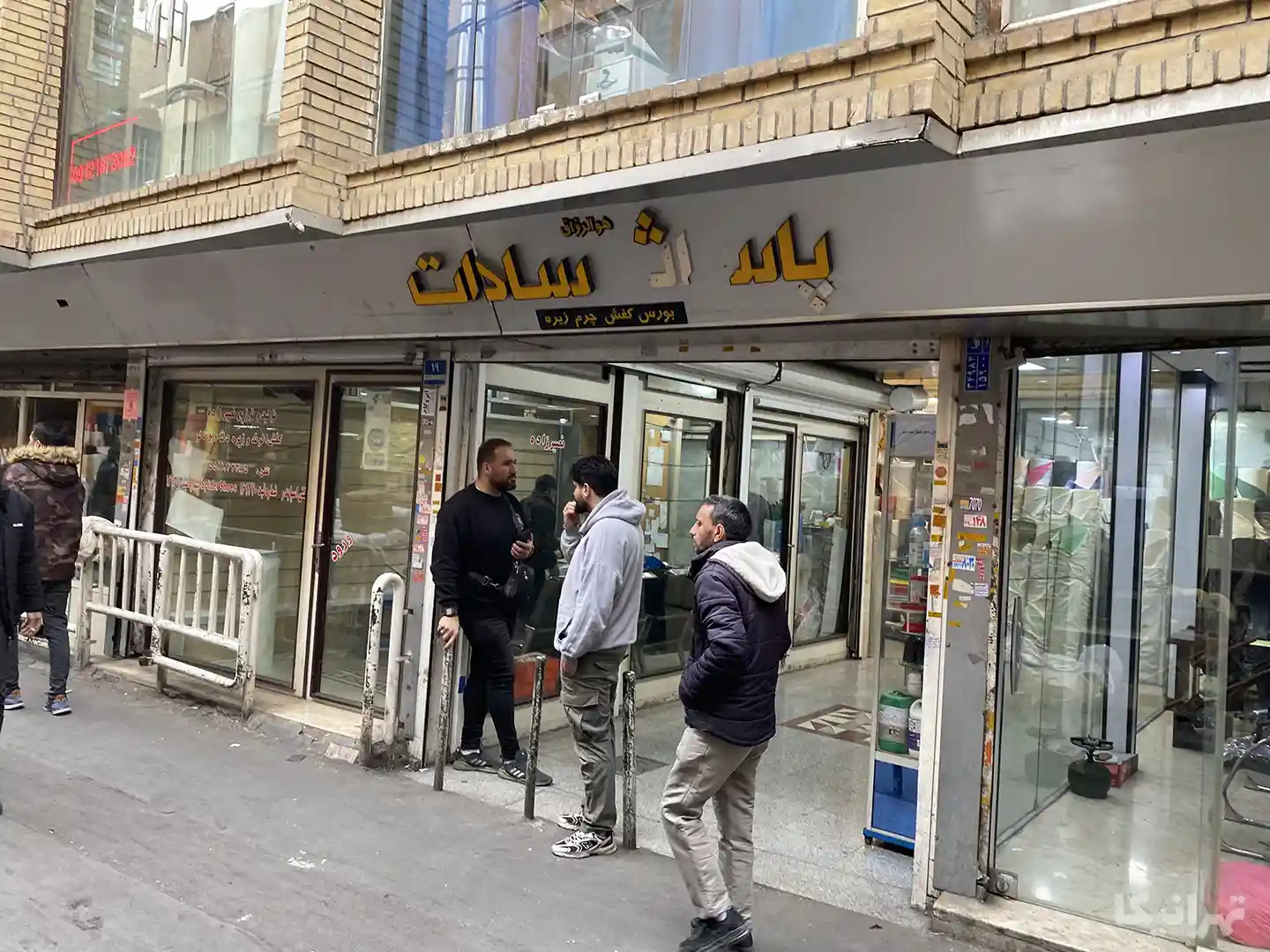 دو مرد در ورودی پاساژ سادات بازار ایستاده و مردان دیگری در حال تردد در کوچه منوچهرخانی