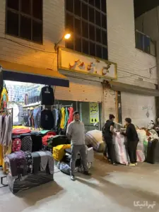 مردی ایستاده و چند نفر در حال بسته‌بندی در مقابل پاساژ قدس بازار