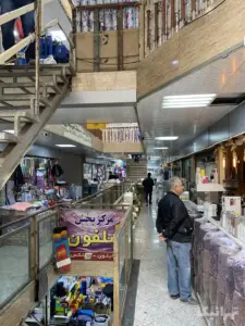 مردی جلوی مغازه‌ای در پاساژ پلاستیک ایستاده است