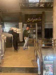 مردی در حال مکالمه با موبایل و مرد دیگری در حال حمل بار در پاساژ کارگری بازار