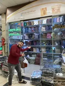مرد فروشنده با خم‌کردن بدنش و نشان دادن داخل مغازه عکاس را به داخل مغازه دعوت میکند