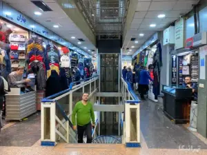 مردم در حال خرید از پاساژ کویتیهای رضایی بازار و مردی در حال بالا آمدن از پله‌ها