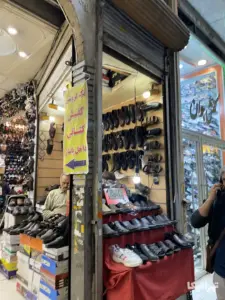 مردی داخل مغازه کوچک کفش‌فروش نشسته است