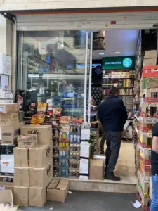 مردی ایستاده در ورودی مغازه موادغذایی خارجی در کوچه معظم‌الدوله بازار